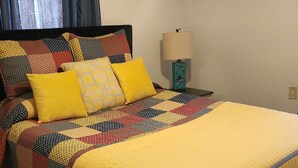 A bed with a yellow quilt and a black headboard, a patterned quilt on the bed, a blue and white lamp, and a patterned rug on the floor. - Blues Alley Downtown Memphis  (Memphis)