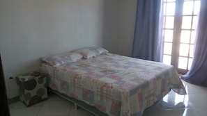 A bedroom with a bed, a suitcase, and a window with curtains.