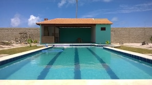 A swimming pool with a tiled deck, a small building with a tiled roof, and a stone wall in the background.