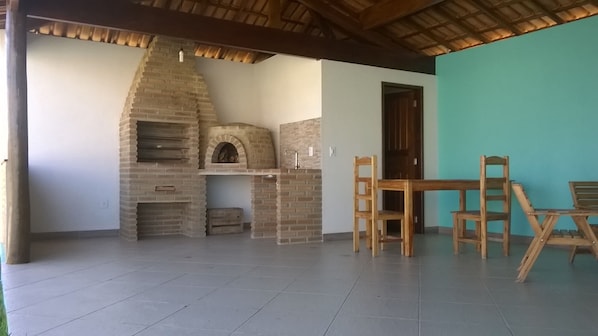 An outdoor patio with a brick oven, wooden chairs, and a table.