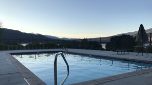 Ein Schwimmbecken mit einer Metallleiter, umgeben von einer Betonplattform und einem Zaun.