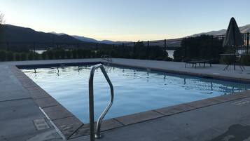 A swimming pool with a metal ladder, surrounded by a concrete deck and a fence.