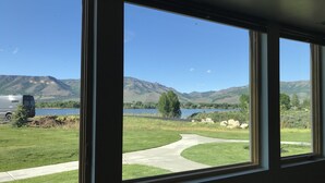 Blick durch große Fenster auf eine Wiese, einen See und Berge.