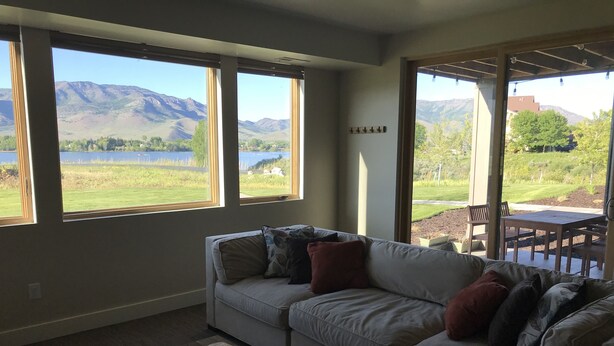 Ein Wohnzimmer mit einer Couch, einem Couchtisch und großen Fenstern mit Blick auf einen See und Berge.