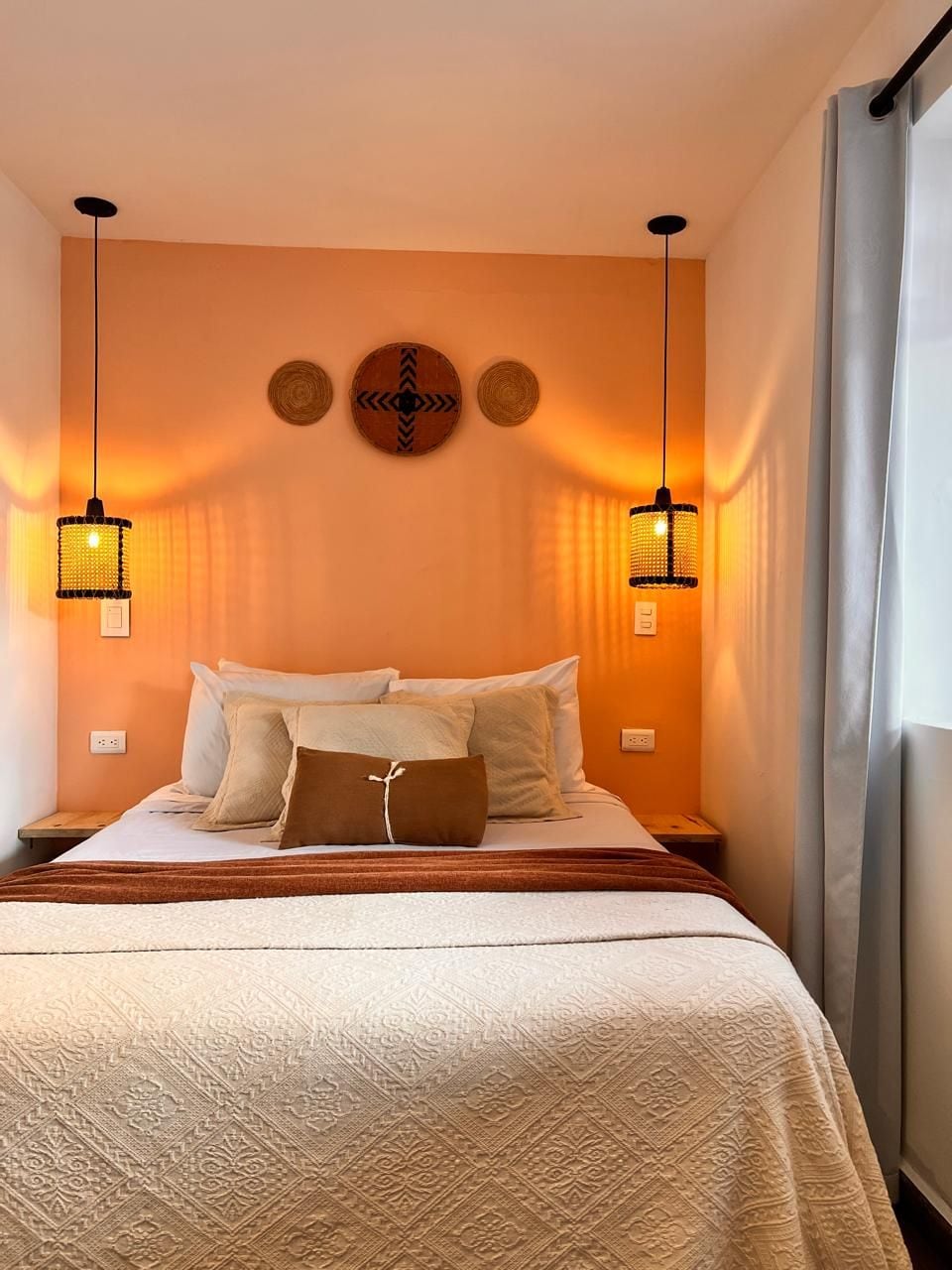 Une chambre d’hôtel avec un lit, deux lampes fixées au mur et un rideau.