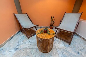 Deux fauteuils confortables avec coussins, une petite table ronde ornée d’un pot de fleurs et un sol carrelé.
