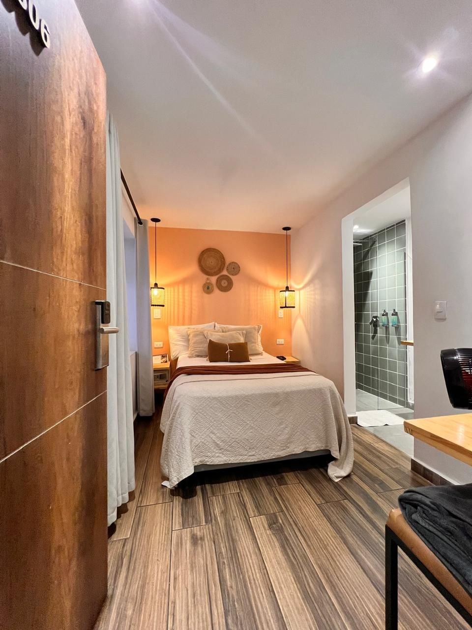 A compact hotel room with a bed, bedside table, and a view of a shower area.