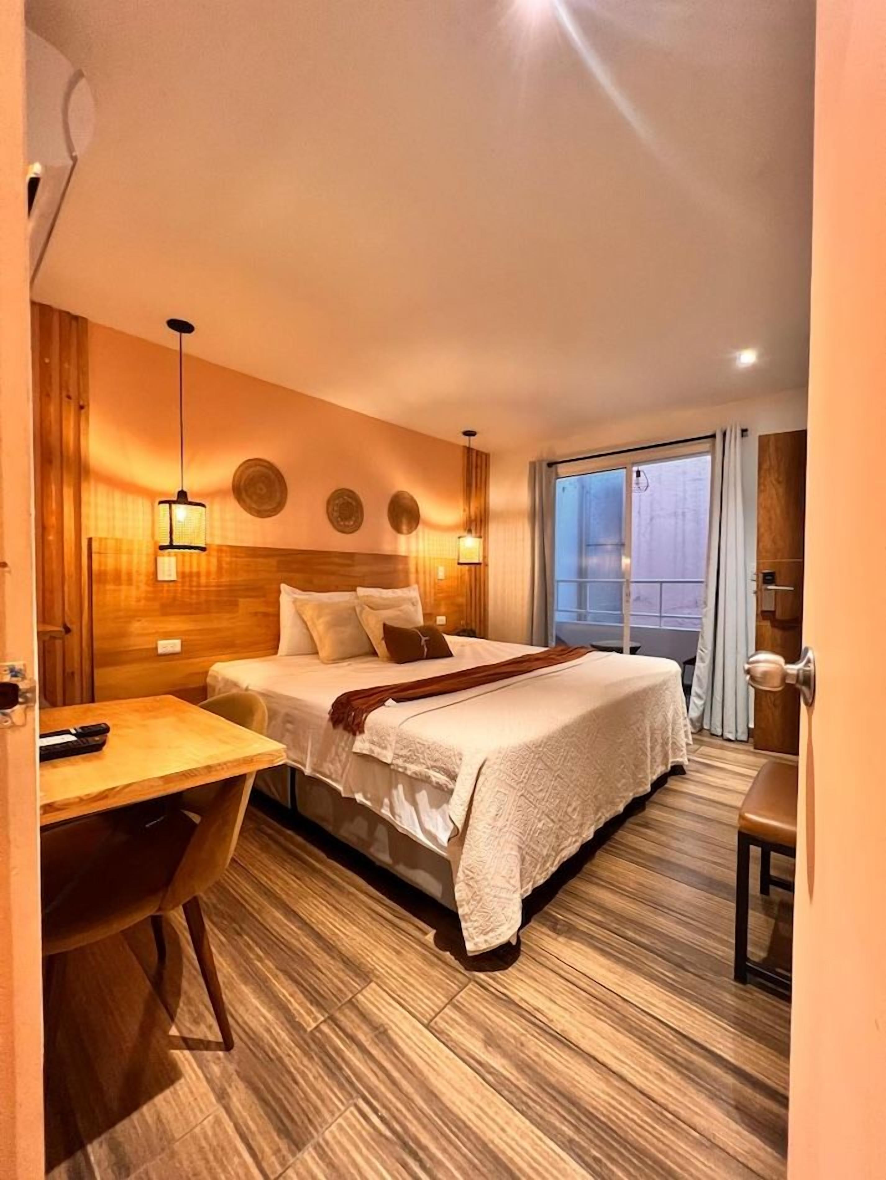 A hotel room with a bed, bedside table, chair, and a window with curtains.