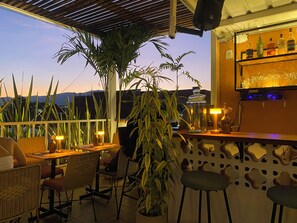 An outdoor seating area with wicker chairs, a table, and a bar with bottles and glasses. - Vivus La Martina Boutique Hotel (Medellín)