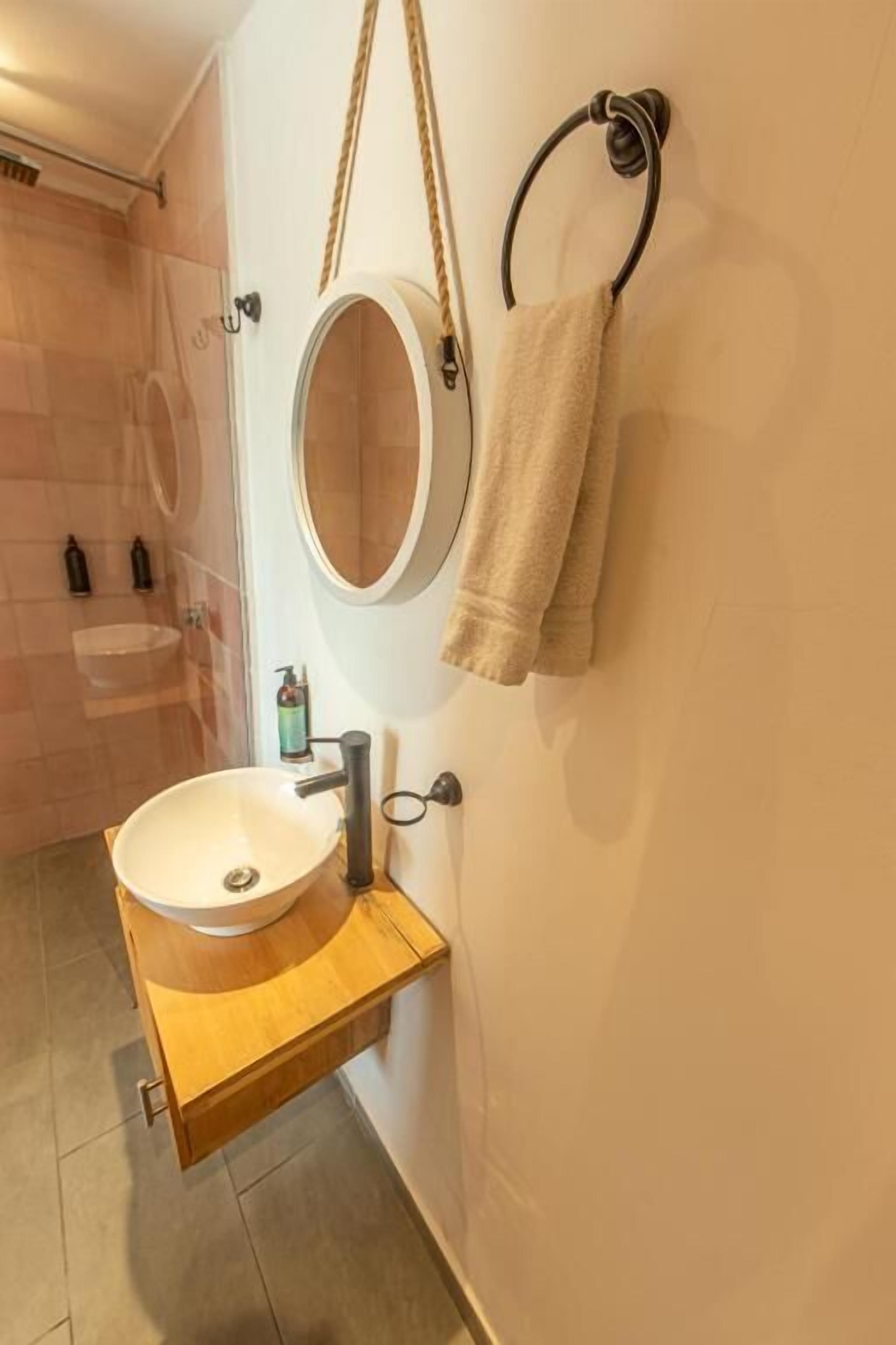 A bathroom with a wooden vanity, a round mirror, and two towels hanging on a towel rack.