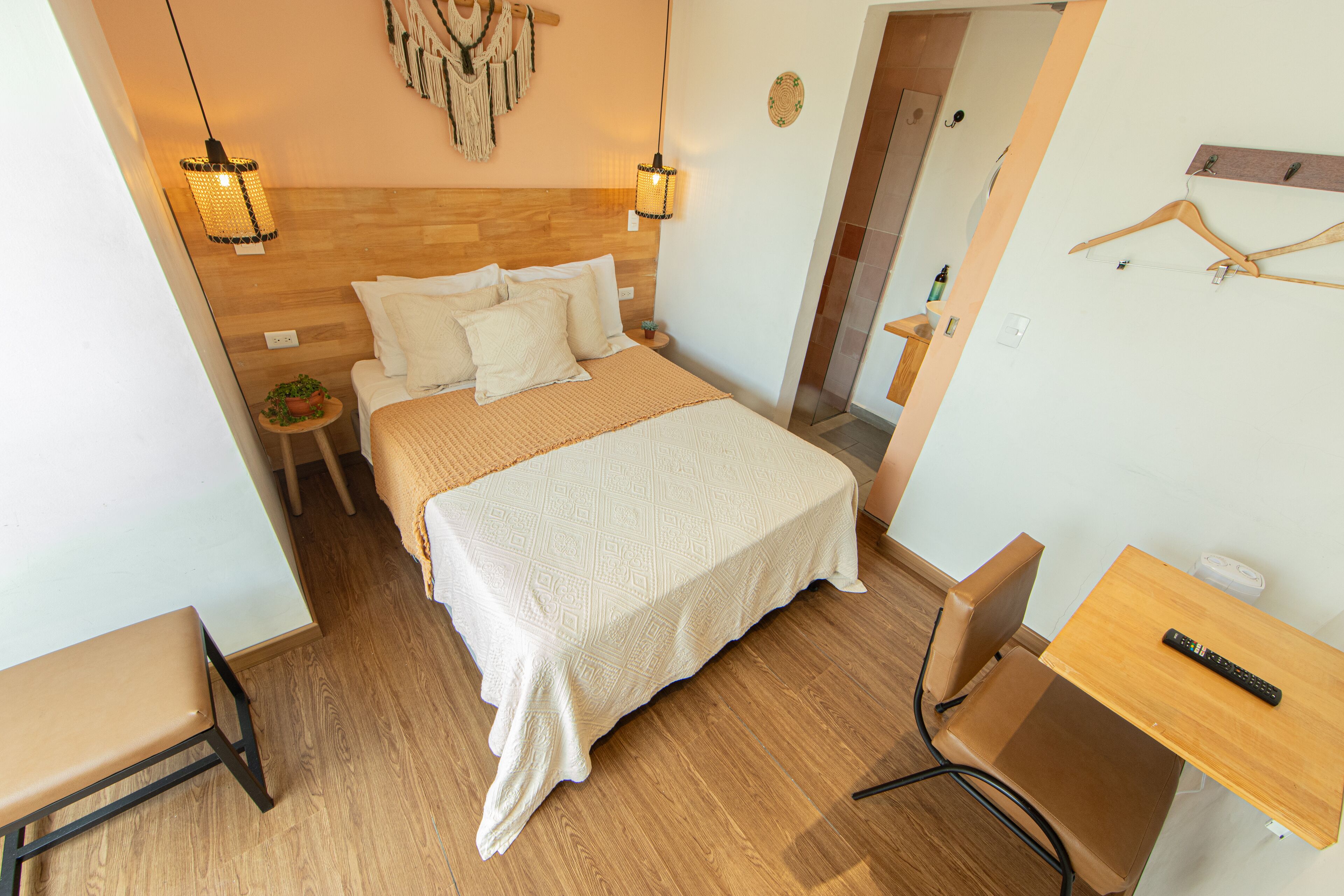 A neatly arranged bedroom with a bed, bedside table, chair, and a small desk with a remote control.