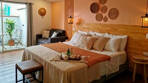 A bedroom with a large bed, a bench, a chair, a small table, and a balcony with a plant. - Vivus La Martina Boutique Hotel (Medellín)