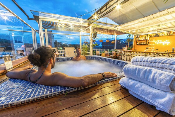 A hot tub with a tiled floor, surrounded by a wooden deck and a glass enclosure.