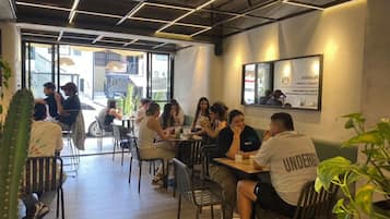 A cafe with tables and chairs, people sitting and eating, and a large window with a view of the street.