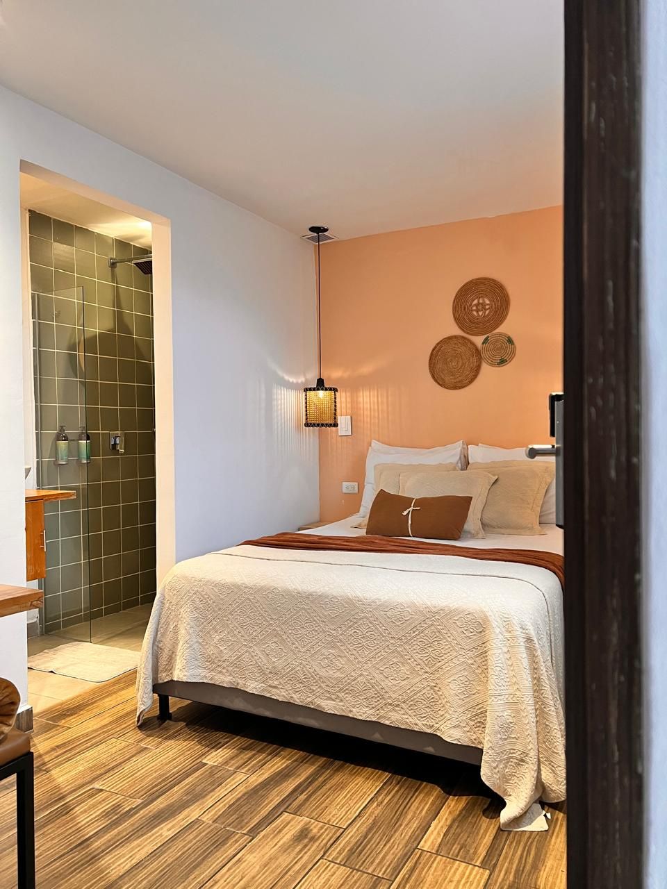 Quarto com cama, mesa de cabeceira, luminária na parede e área de chuveiro.