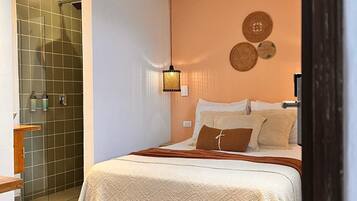 A bedroom with a bed, a nightstand, a wall-mounted lamp, and a shower area.