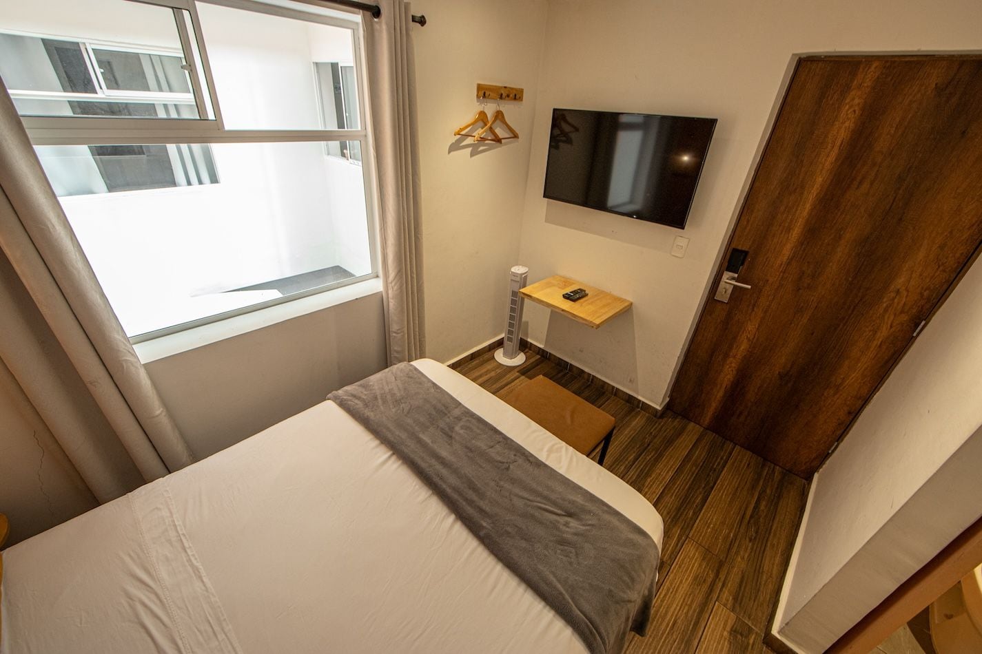 Un dormitorio con una cama, televisor montado en la pared, una mesita de noche y un ventanal.