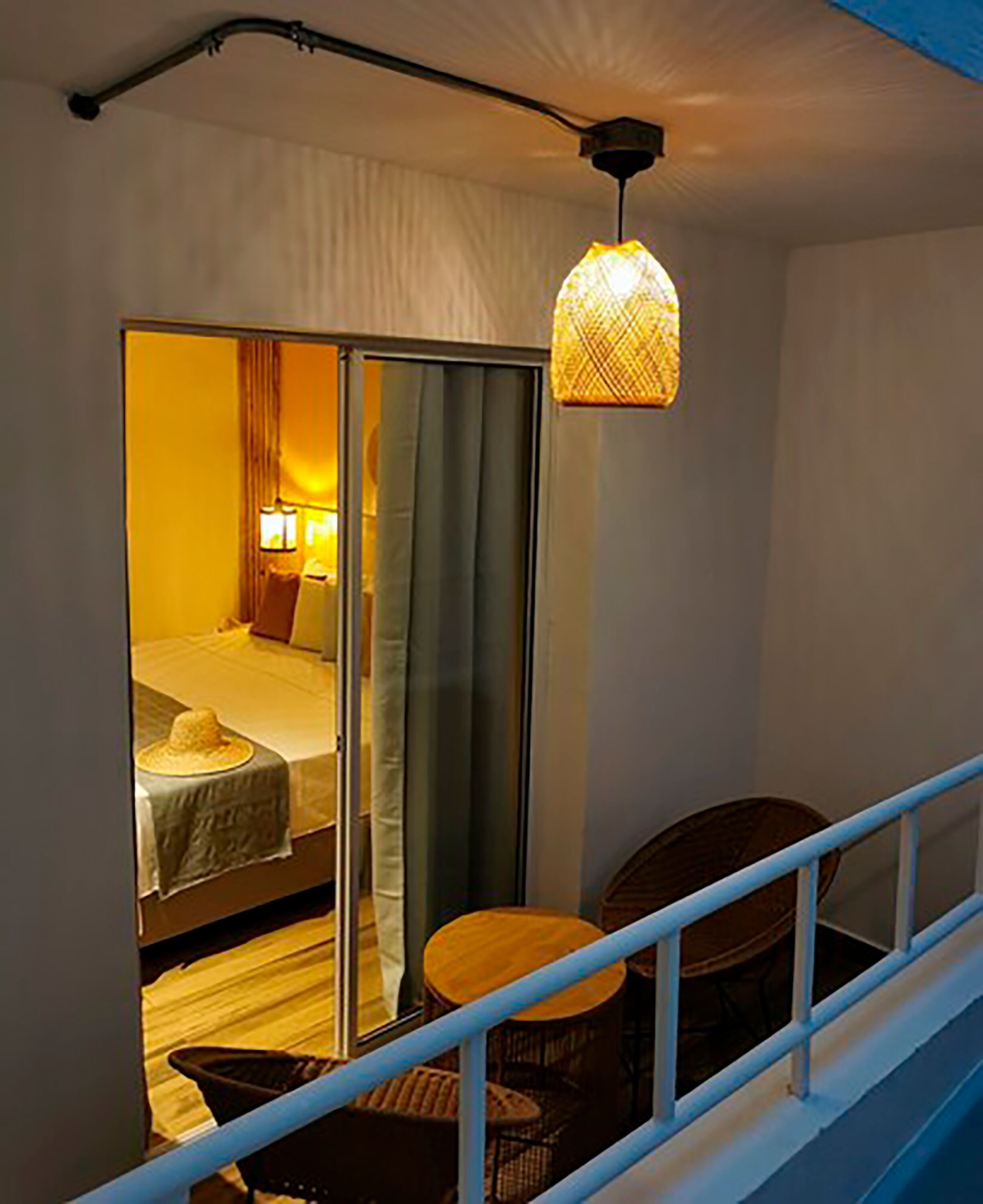 Un balcón con cama y mesa, un lámpara colgante y vista a una habitación con cortinas.