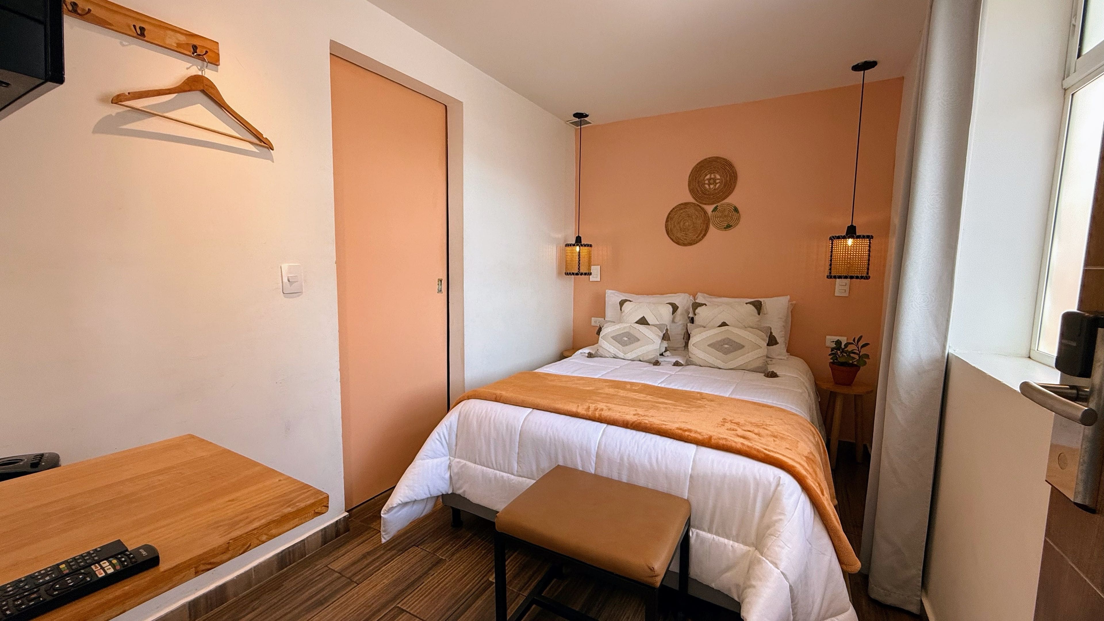 A bedroom with a bed, bedside table, hanging clothes rack, and a window with curtains.