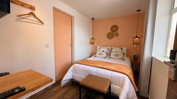 A bedroom with a bed, bedside table, hanging clothes rack, and a window with curtains.