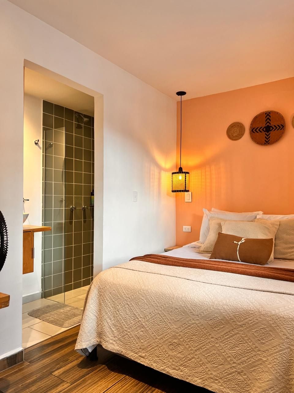 A bedroom with a bed, a bedside table, a lamp, a shower, and a wall-mounted clock.