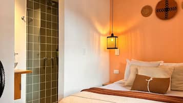 A bedroom with a bed, a bedside table, a lamp, a shower, and a wall-mounted clock.