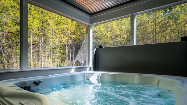 A hot tub with a waterfall feature, large windows, and a view of a forest. - Hot tub-Interactive family gaming-Game room! (Helen)