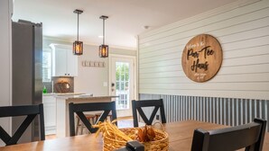 A dining area with a wooden table, black chairs, and a woven basket with onions. There is a sign on the wall that reads "Welcome to the Par-Tee Haus." - Hot tub-Interactive family gaming-Game room! (Helen)