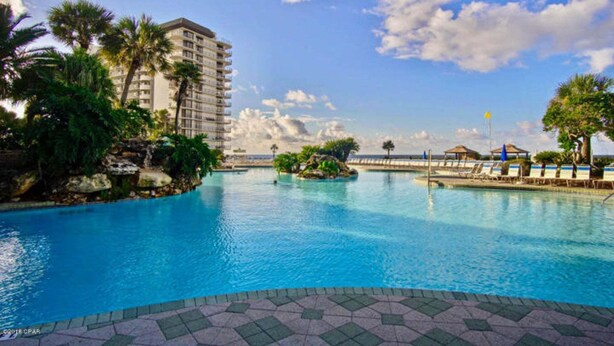 Ein Hotelpoolbereich mit großem Pool, Palmen und einem Gebäude im Hintergrund.