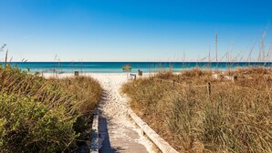 Ein Strandweg führt zum Meer, mit einem Holzsteg und grasbewachsenen Dünen.