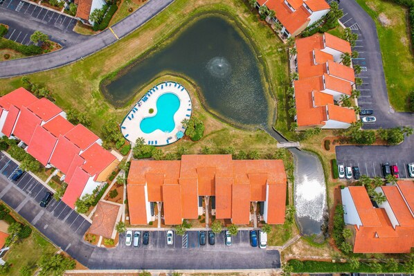 An aerial view of a residential area with a swimming pool, multiple red-roofed buildings, and a parking lot.