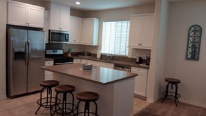 A modern kitchen with white cabinets, stainless steel appliances, a central island with stools, and a window with blinds. - LOWEST PRICE OF THE SEASON! 
NEW and AMAZING! Spacious! DOD, Military Welcome! (Imperial Beach)