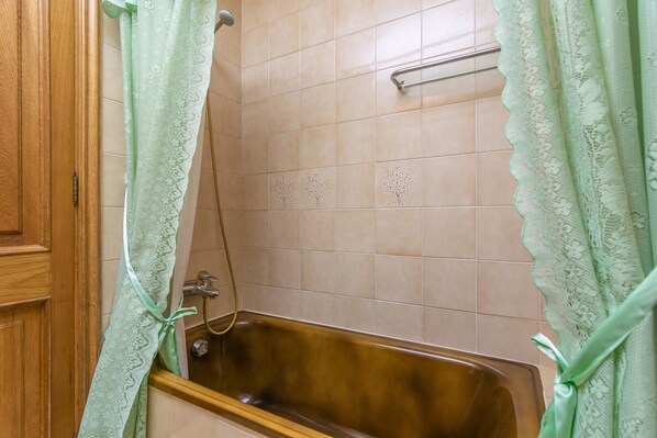 Un baño con puerta de madera, una bañera y cortinas de encaje verde.