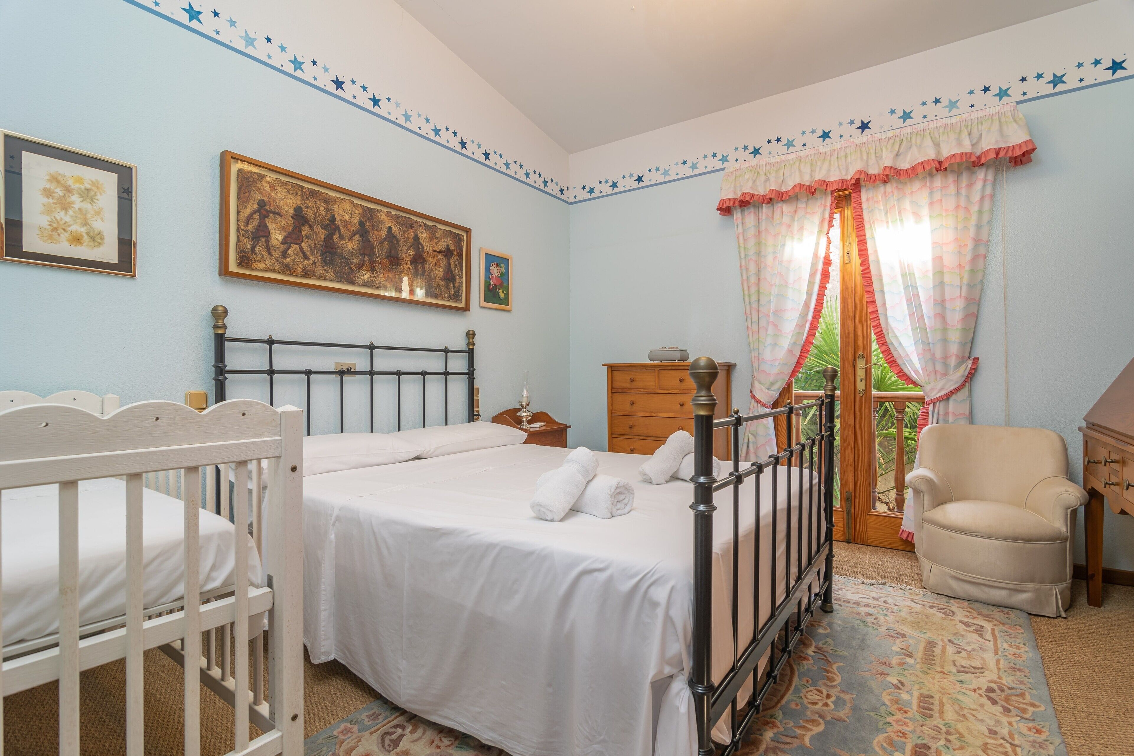 Un dormitorio con cama, cuna, silla y ventana con cortinas.