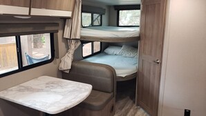 A compact RV interior with a bunk bed, a small dining table, and a window with a view of the outside. - Family Fun "Campout" (Saint George)
