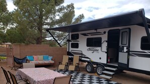 An RV with a covered porch area, a dining table with chairs, and a checkered outdoor rug. - Family Fun "Campout" (Saint George)