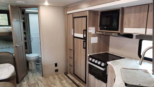 A compact kitchen with a microwave, stove, sink, and a toilet visible through an open door. - Family Fun "Campout" (Saint George)