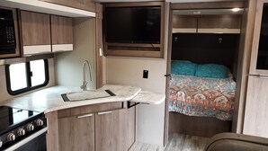 A compact RV kitchen with a stove, sink, and window. - Family Fun "Campout" (Saint George)