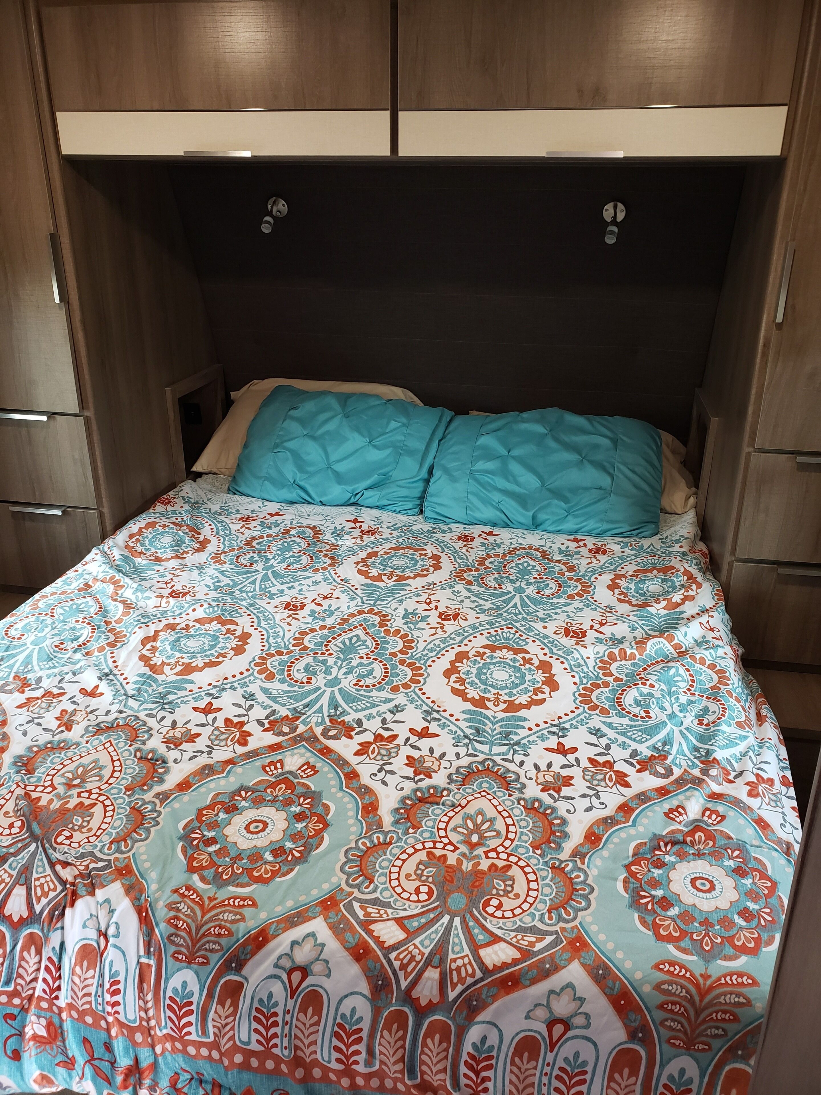 A bed with a patterned bedspread, two pillows, and a wooden headboard.