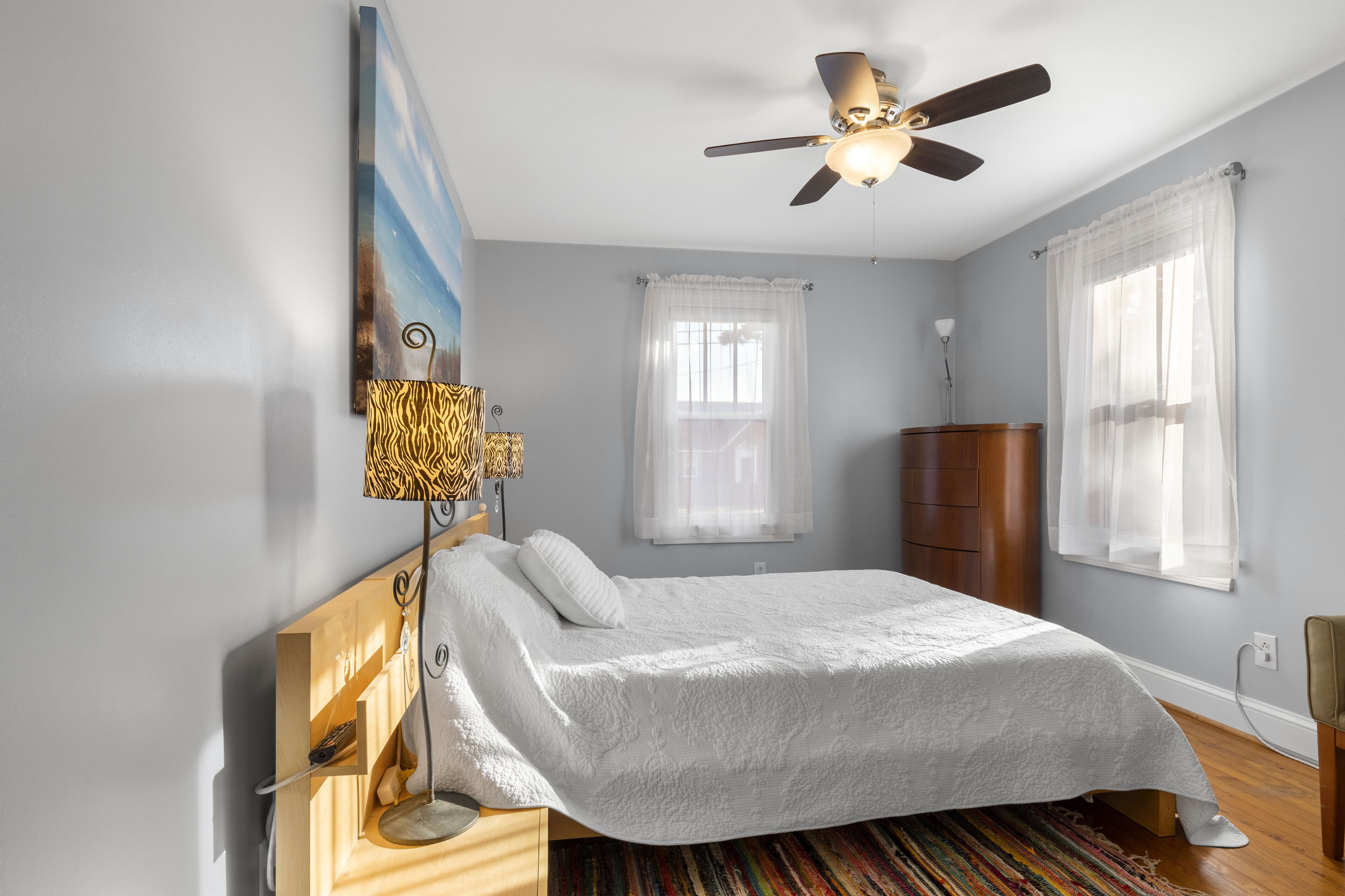Une chambre à coucher avec un lit, un ventilateur de plafond, une lampe et une fenêtre avec des rideaux.