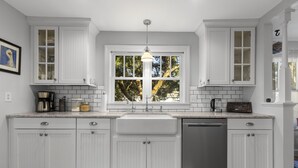 Een keuken met witte kasten, een groot raam en een hanglamp.