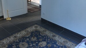 A hallway with a patterned rug, a white door, and a staircase in the background.