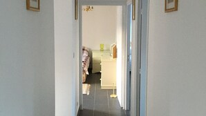 A hallway with a chandelier, framed pictures on the walls, and a bed in the background.