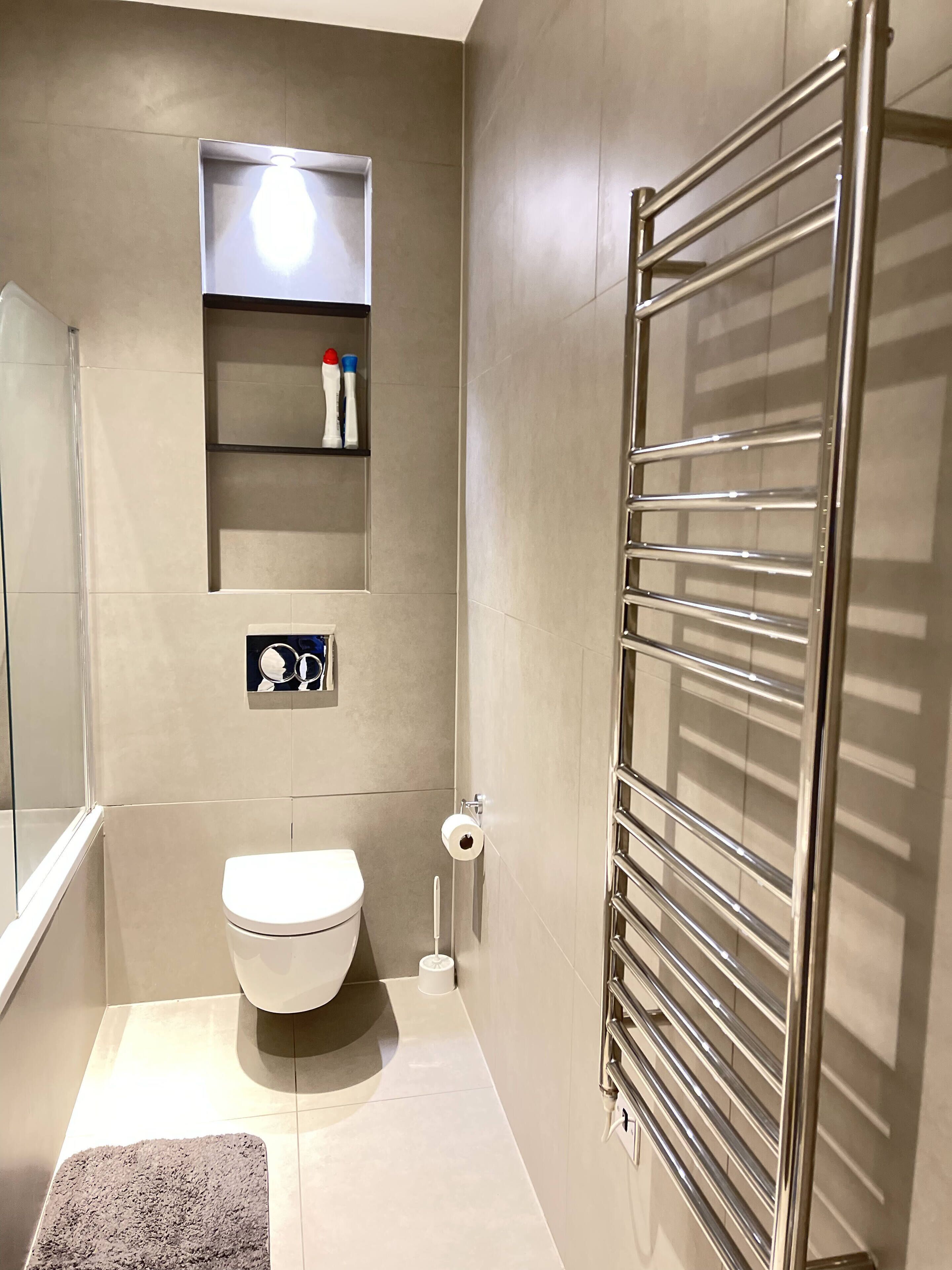 Une salle de bain moderne comprenant des toilettes, une étagère avec des articles de toilette, un porte-serviettes et une cabine de douche en verre.