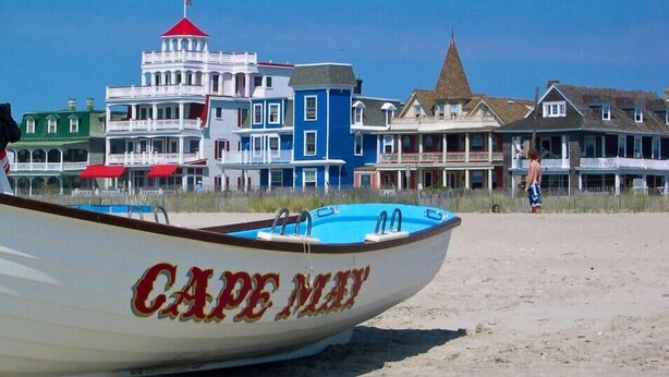 Une plage avec un bateau appelé « Cape May » et des bâtiments colorés en arrière-plan.
