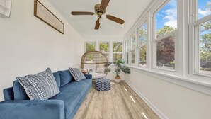 Une pièce spacieuse avec un canapé bleu, un ventilateur de plafond, de grandes fenêtres et un plancher en bois.