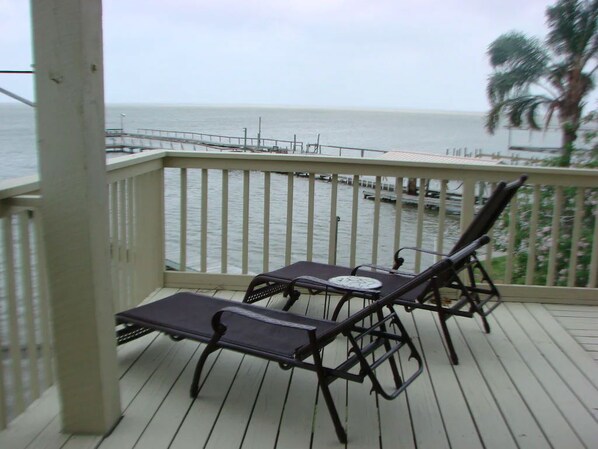 A wooden deck with two lounge chairs and a table, overlooking a calm sea and a pier. - Exceptional Waterfront Home with 165 foot fishing pier (Rockport)