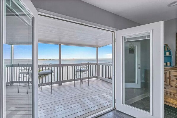 A wooden deck with a glass door leading to a room, overlooking a body of water.