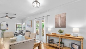 Un coin repas avec une table et des chaises en bois, un ventilateur de plafond et une vue sur l’extérieur grâce à des portes vitrées.