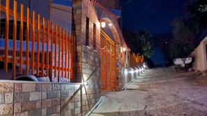 A building with a stone facade, a gated entrance, and a paved pathway leading to the entrance. - Iliaktis Xenios Zeus  (Νήσοι)